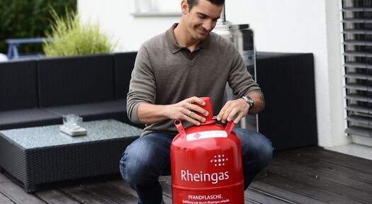 Mann sichert seine 11 kg Gasflasche von Rheingas mit roter Verschlusskappe, um sie richtig zu lagern.